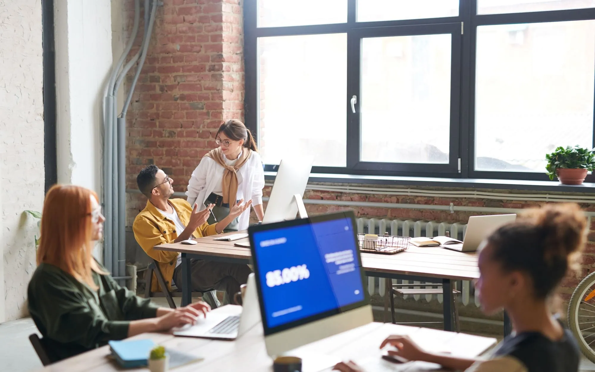 A team working together around laptops in a bright, brick-walled office