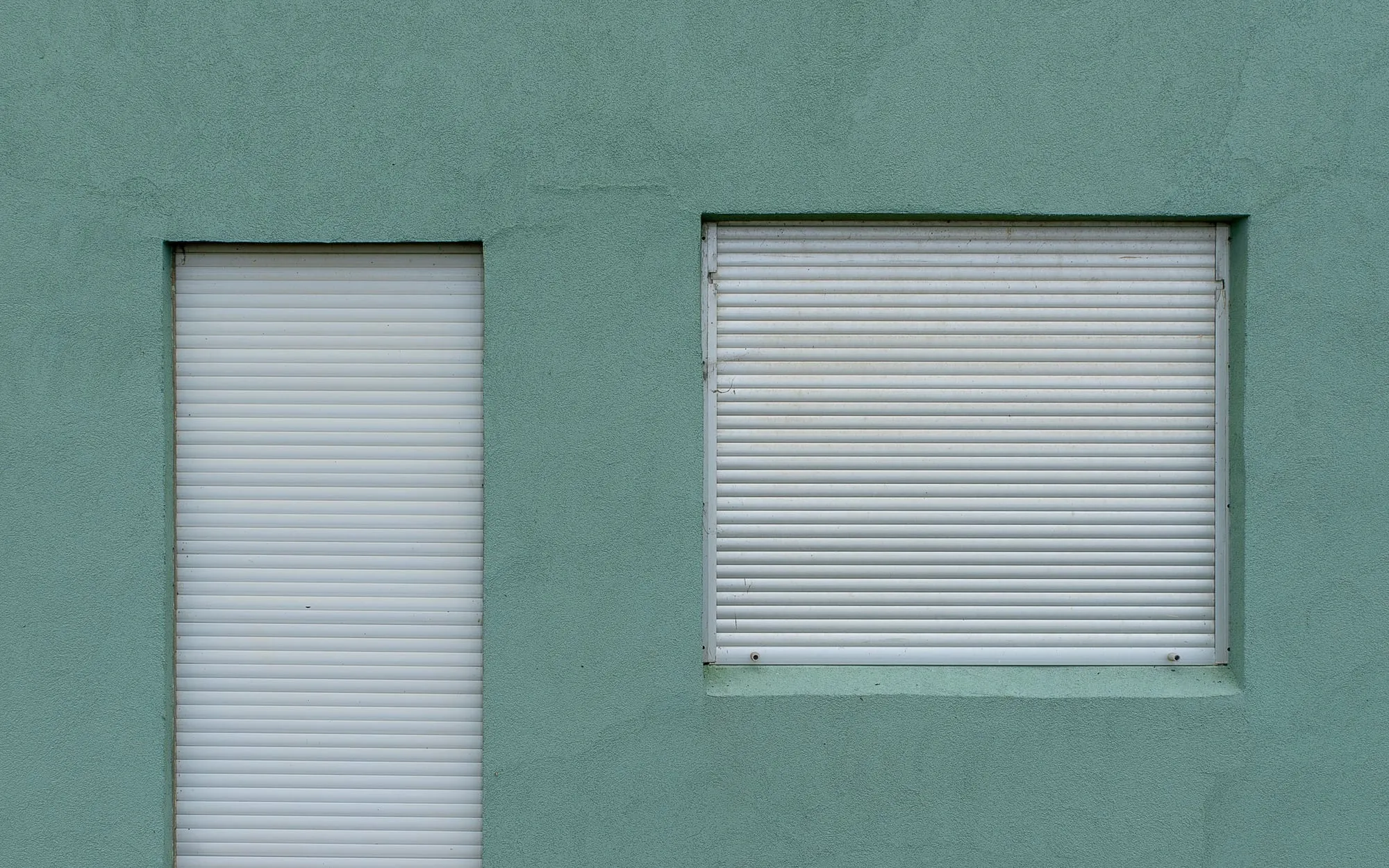 Two white shutters on a plain sage-green wall