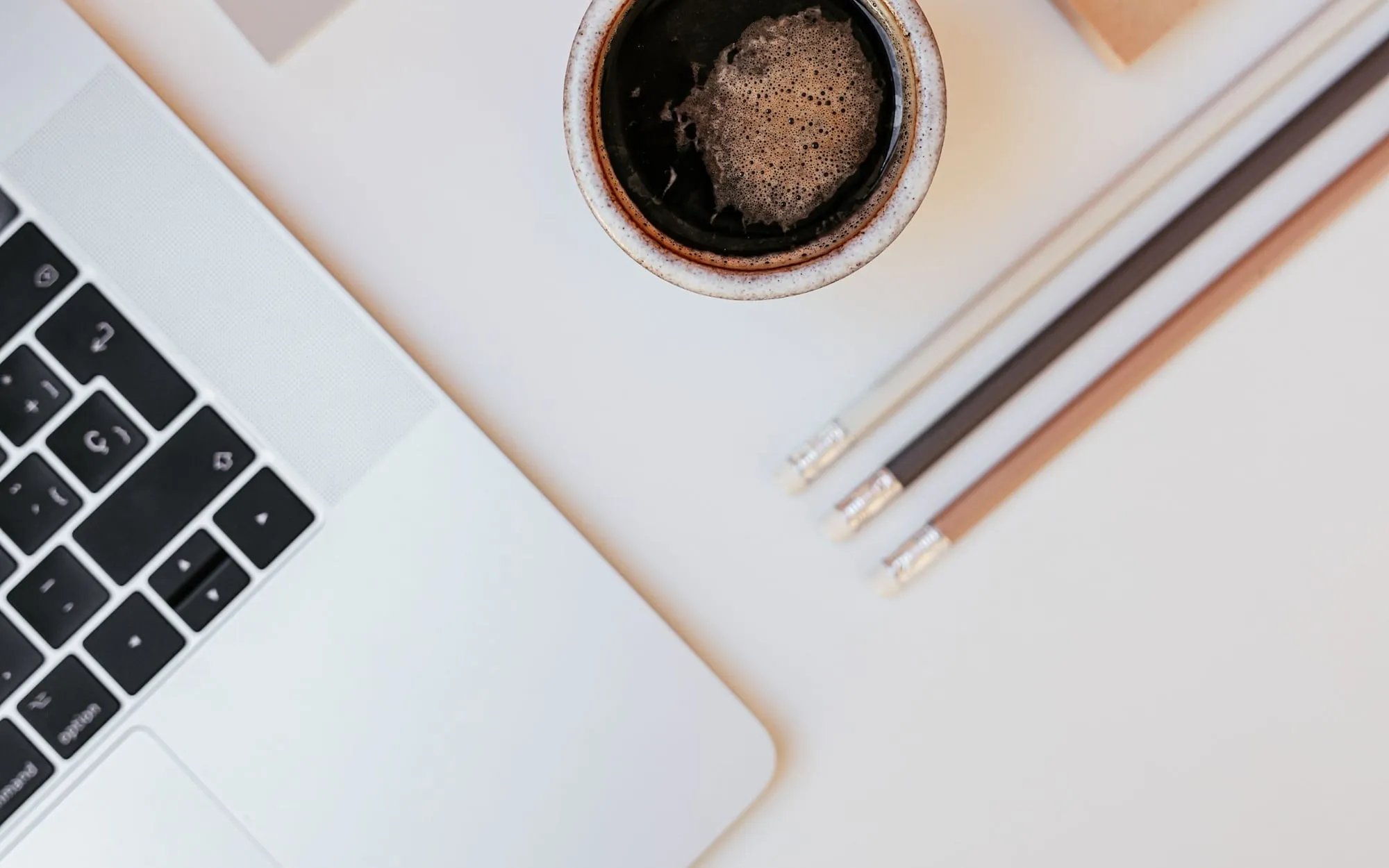 A cup of coffee, a laptop and pencils on a white desk, seen from above
